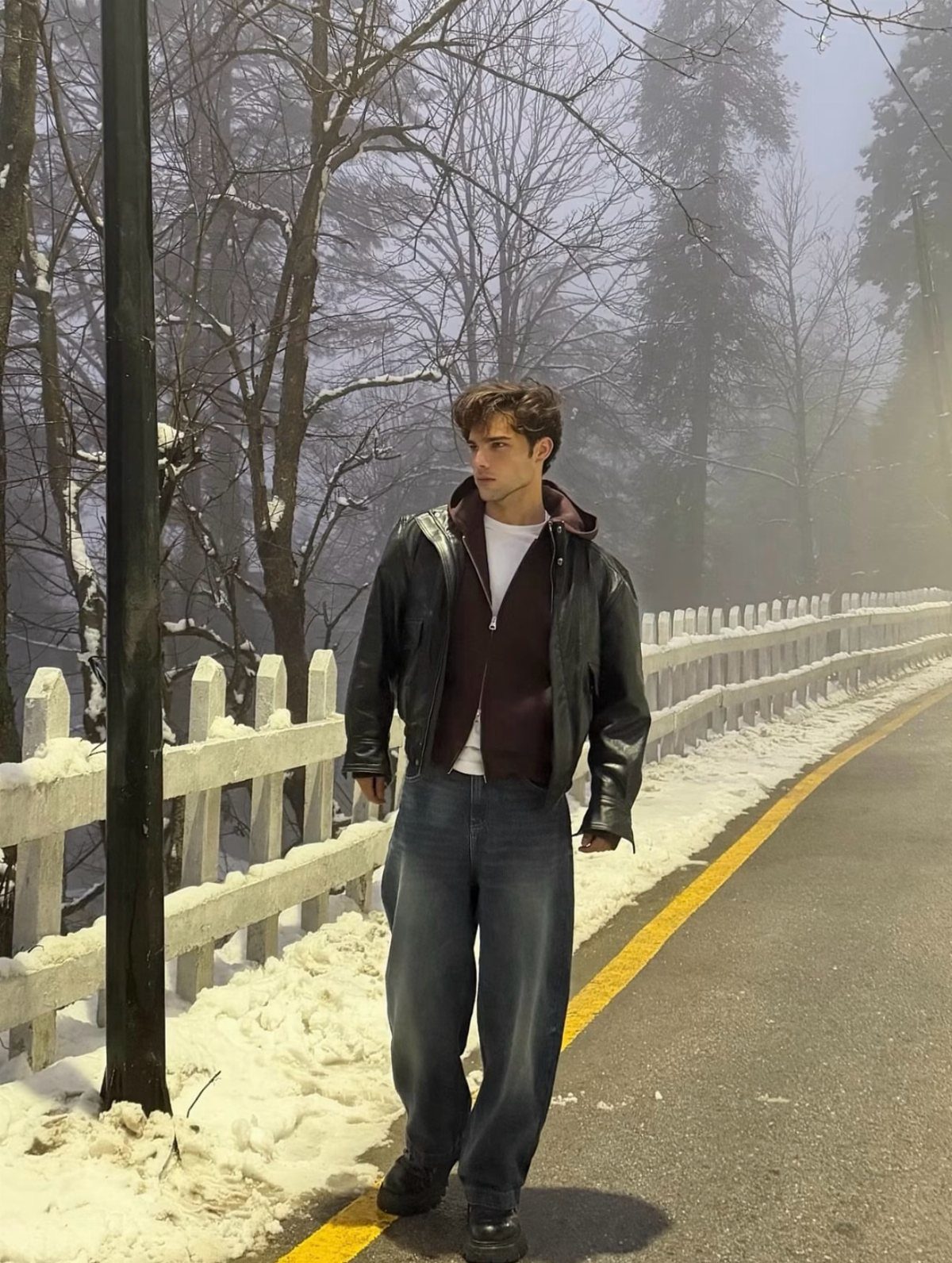 Man in black leather jacket and maroon hoodie standing on snowy road