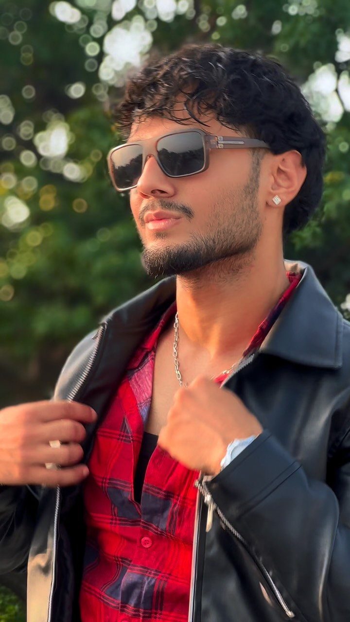 Man wearing a black leather jacket over a red and black plaid shirt.