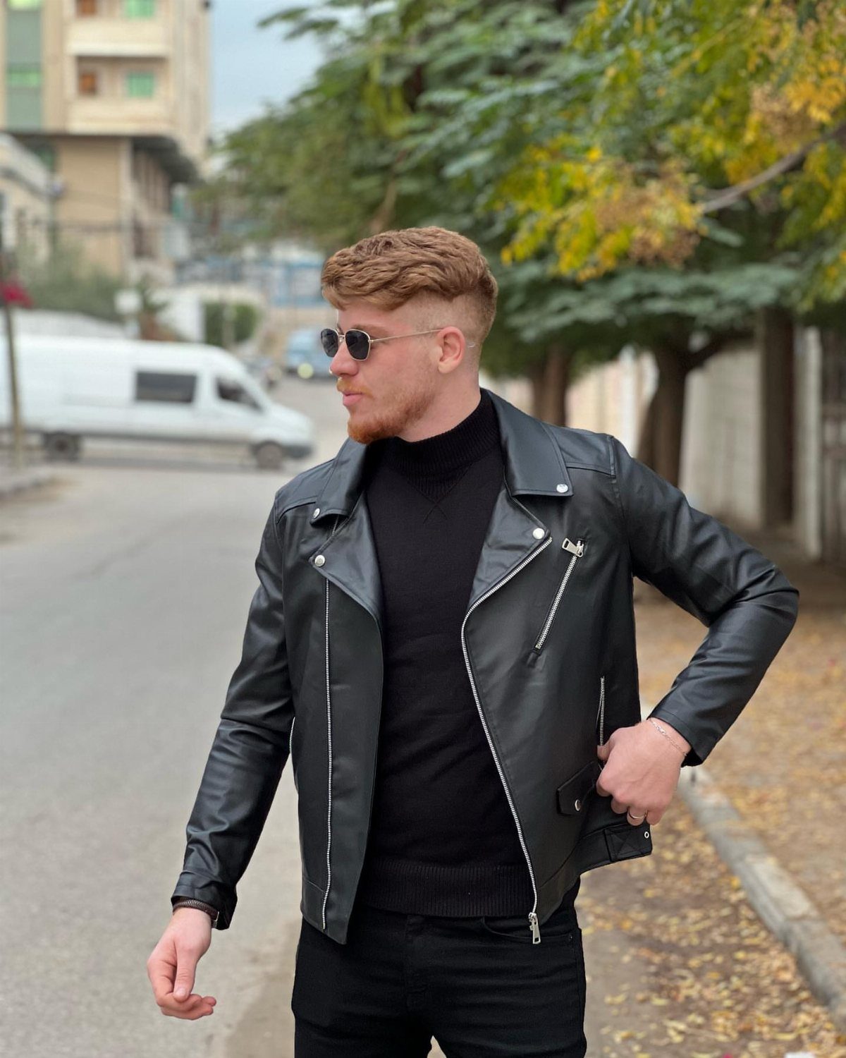 Man wearing a black leather biker jacket and sunglasses on a city street