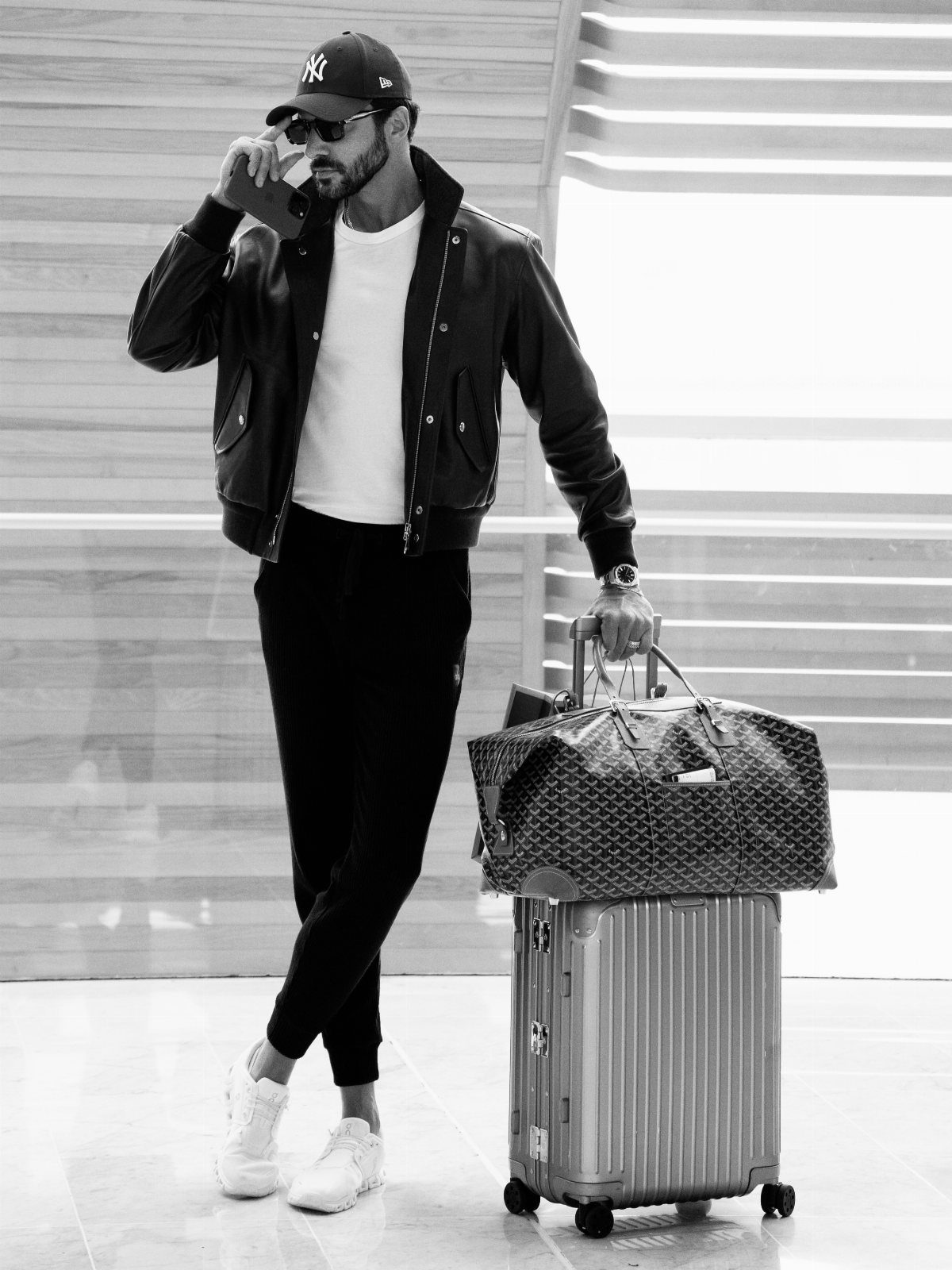 Man in leather bomber jacket and baseball cap standing with travel luggage