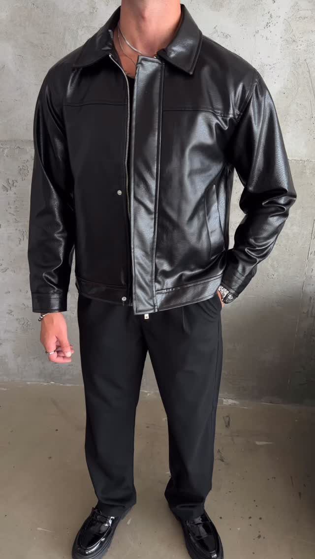 Man wearing a black leather jacket, black pants, and black loafers against concrete.
