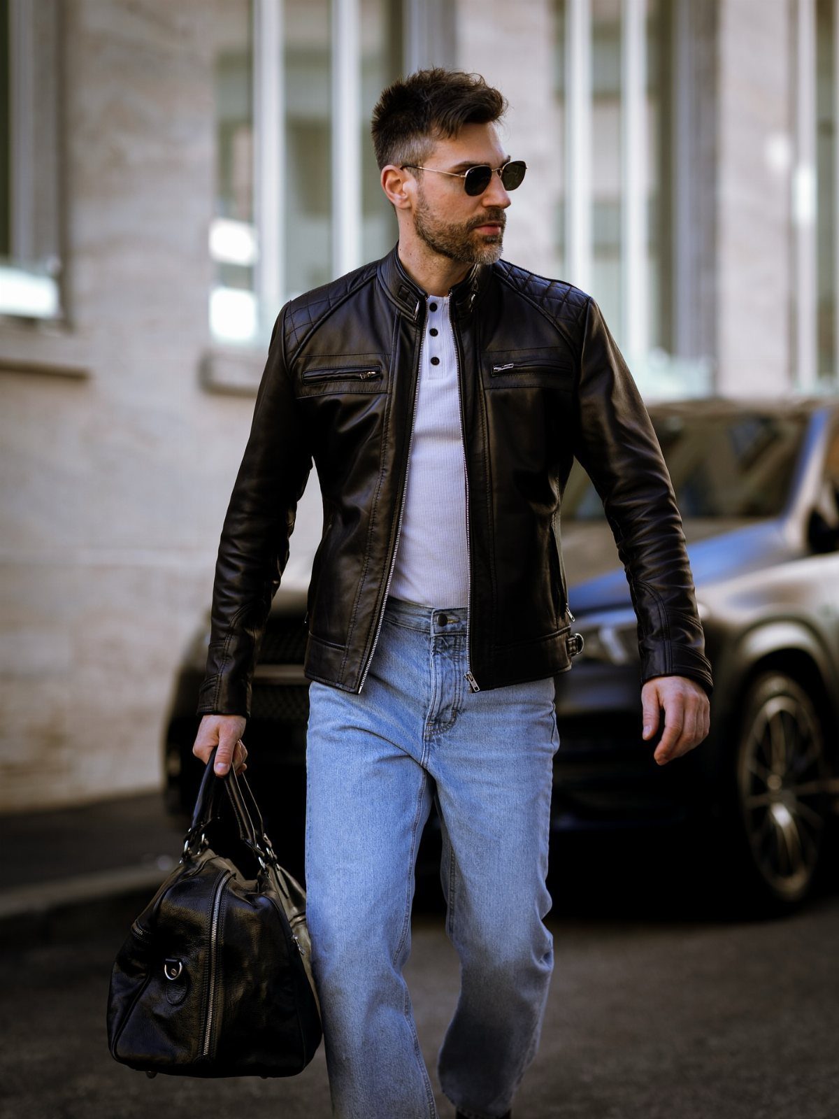 Man in black leather jacket and white shirt wearing light blue jeans