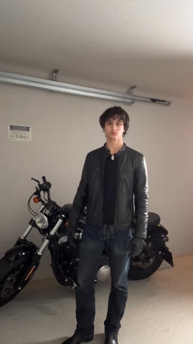 Man in black leather jacket and jeans posing with a black motorcycle