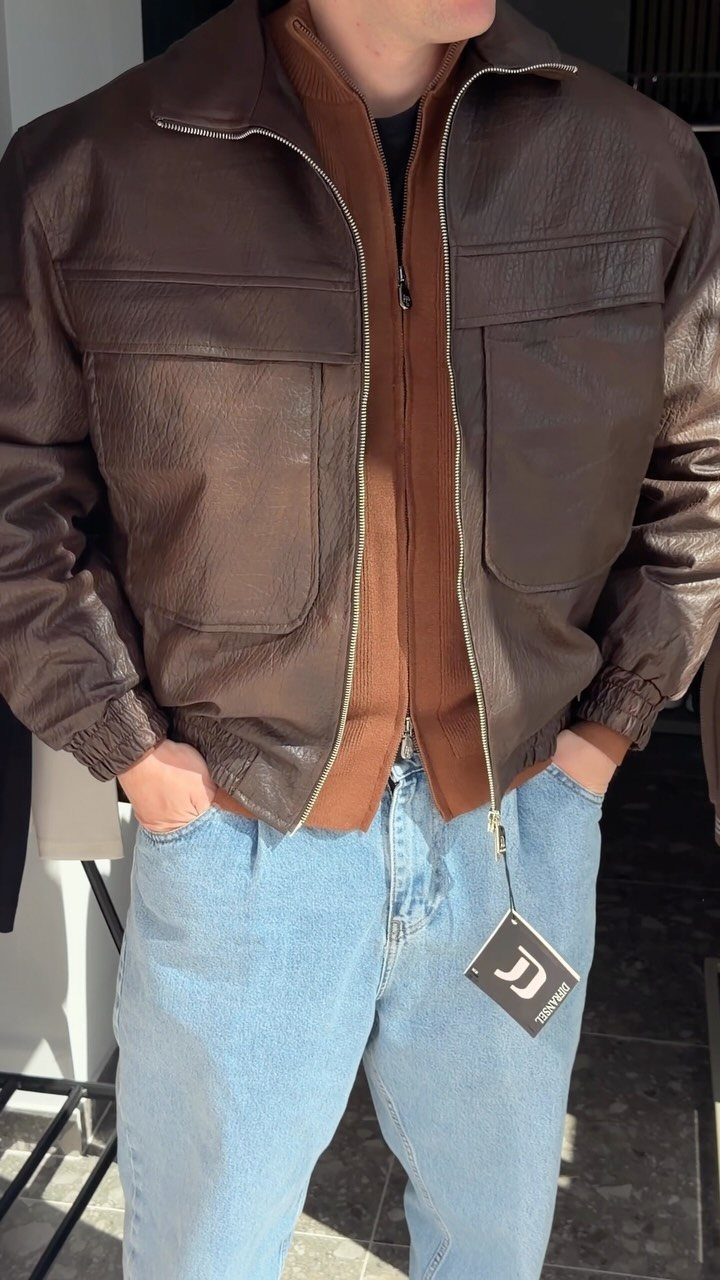 Person wearing a brown leather jacket layered over a brown sweater and blue jeans