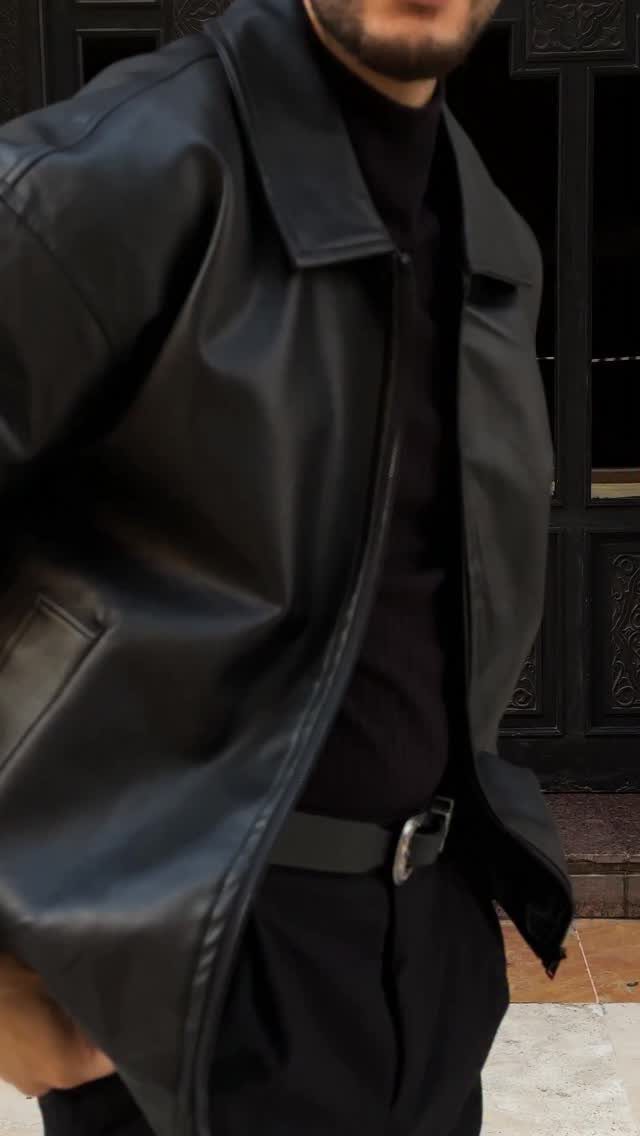 Man wearing an oversized black leather jacket with a black turtleneck and trousers.