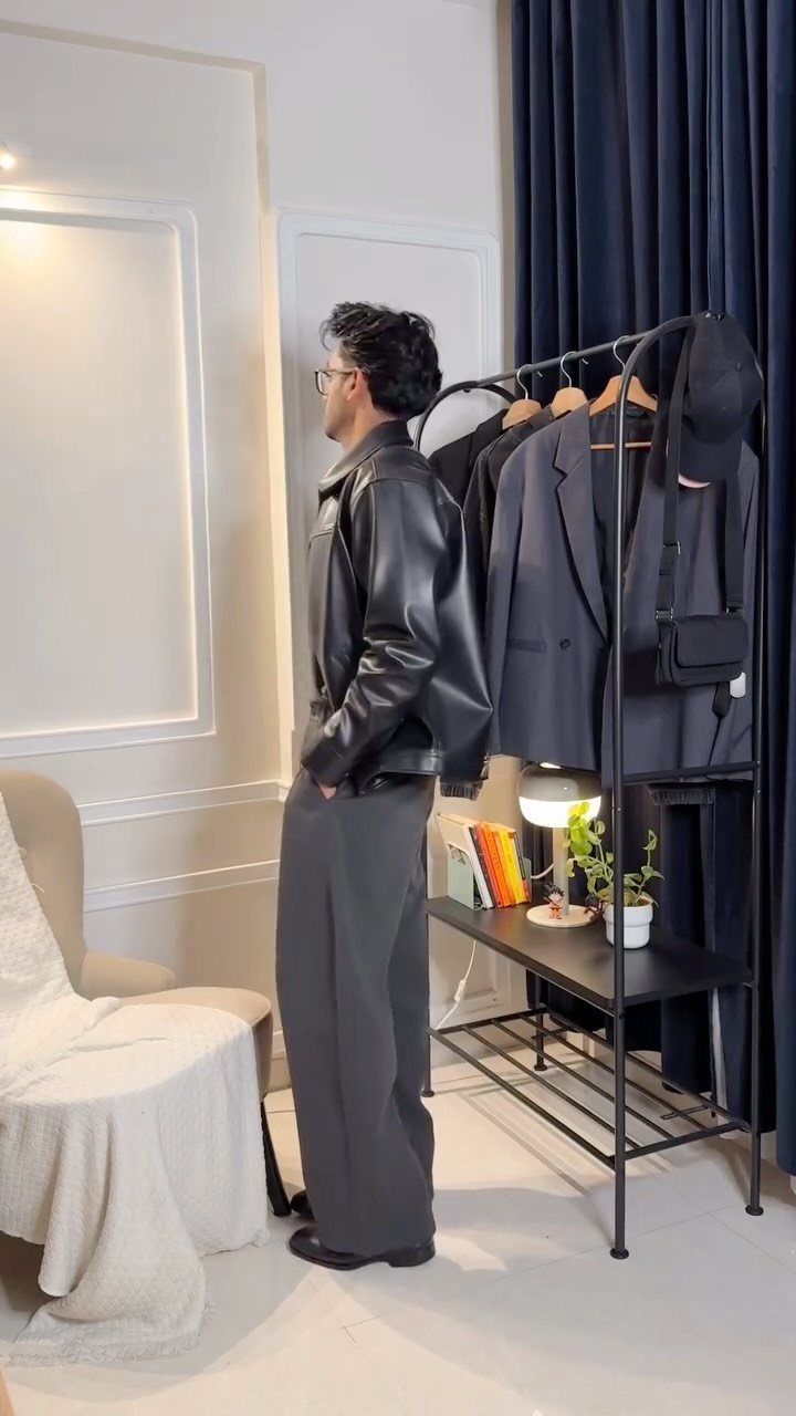Man wearing a black leather jacket and grey trousers standing by a clothing rack