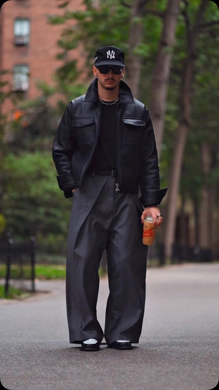 Man wearing a black leather jacket and wide-leg grey trousers on a city street