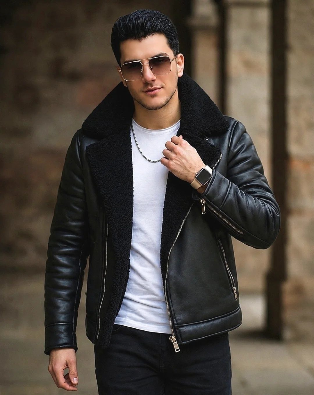 Man wearing a black leather shearling jacket, white t-shirt, and black pants outdoors.