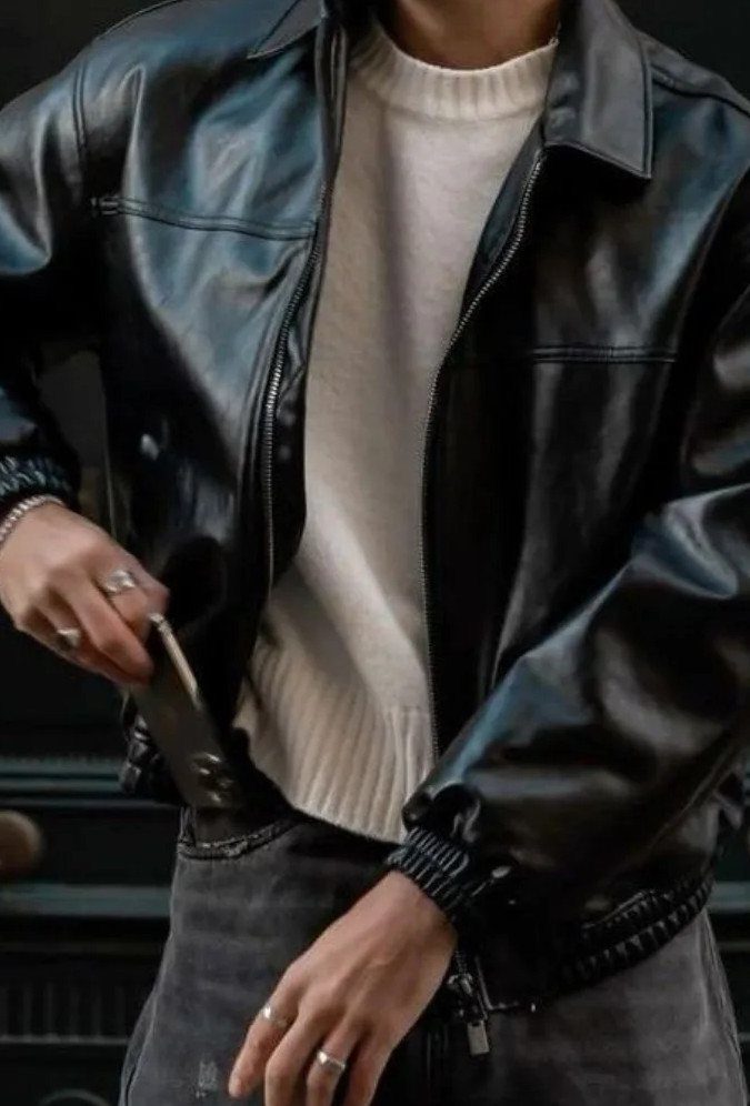 Person wearing a black leather jacket over a white ribbed sweater and grey jeans.