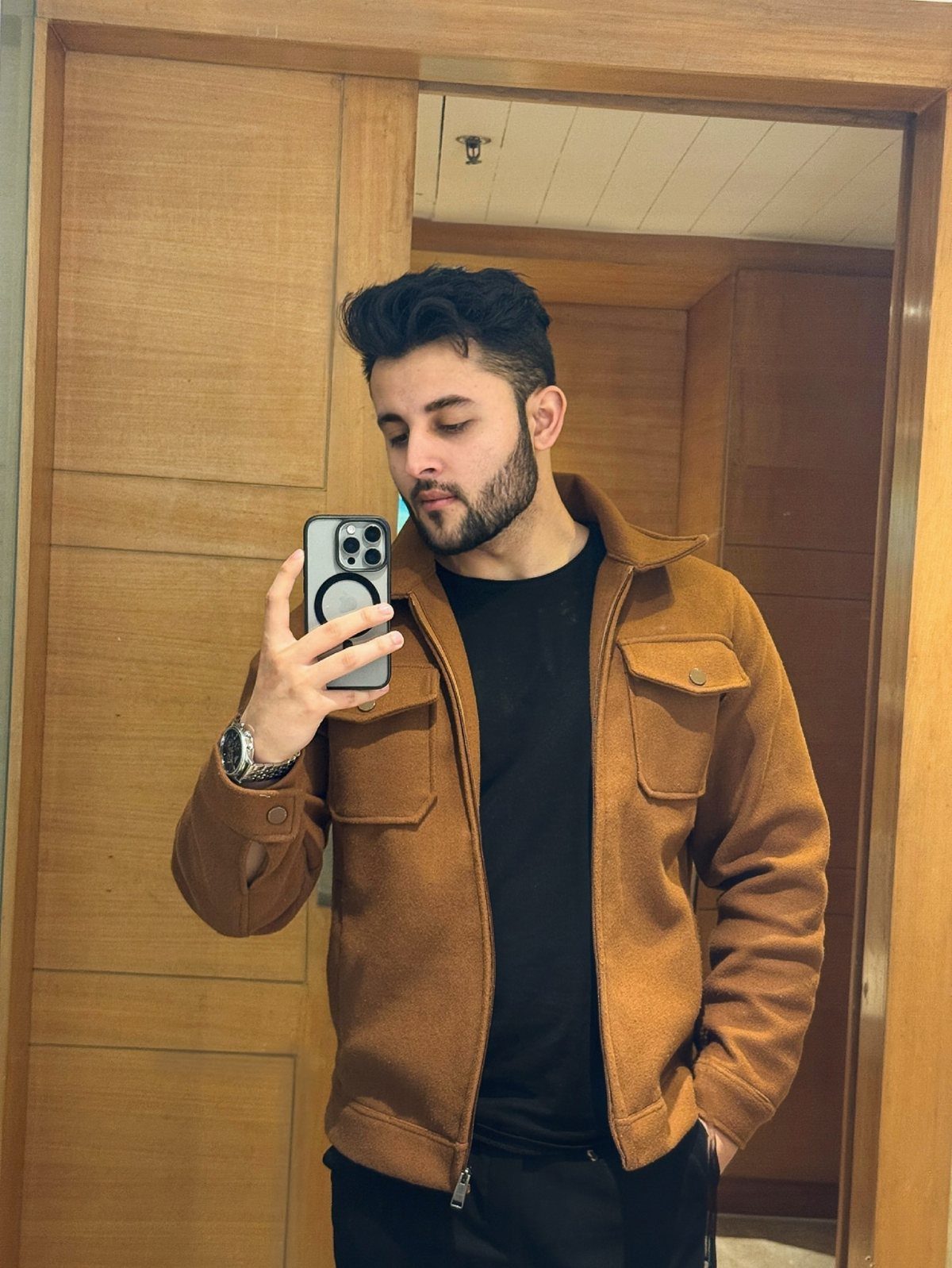 Man wearing a light brown jacket over a black t-shirt in a mirror selfie.