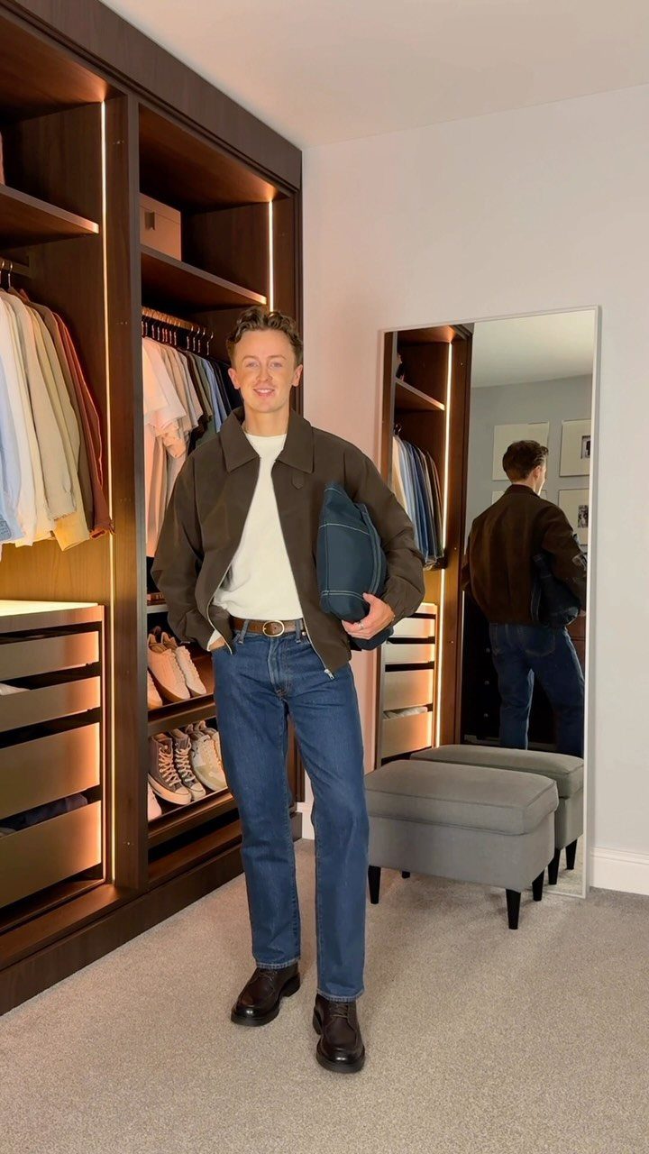 Man wearing a brown jacket, white shirt, blue jeans, and dark brown boots.