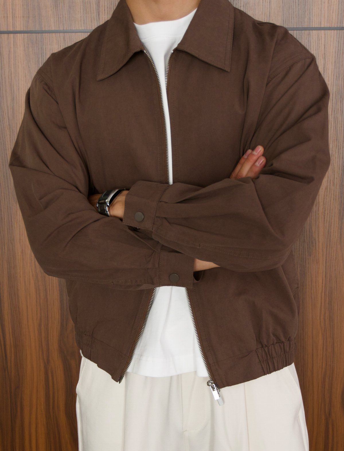 Person wearing a brown jacket with a white shirt and off-white trousers.