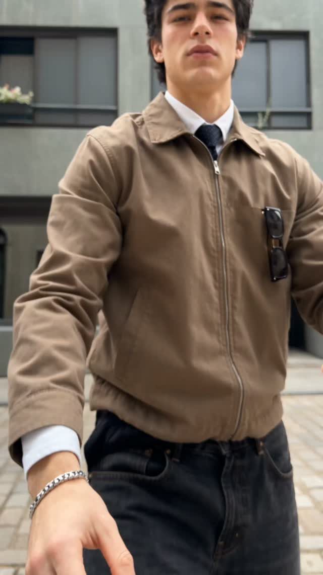 Man wearing a light brown jacket, white shirt, dark tie, and black trousers.