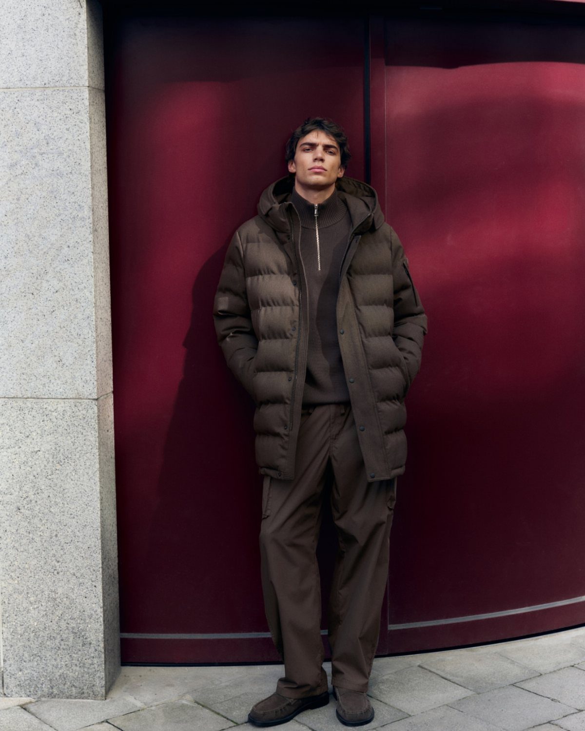 Man wearing a monochrome brown puffer jacket, sweater, and matching trousers outdoors.