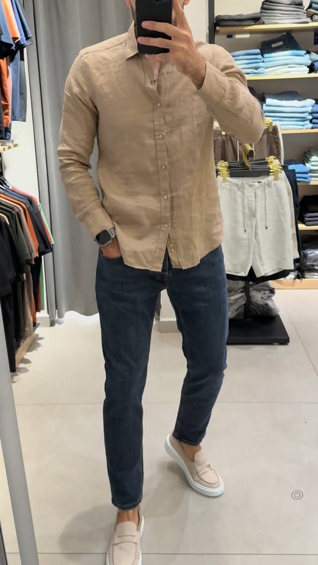 Man wearing a tan linen shirt, dark blue jeans, and beige slip-on shoes.