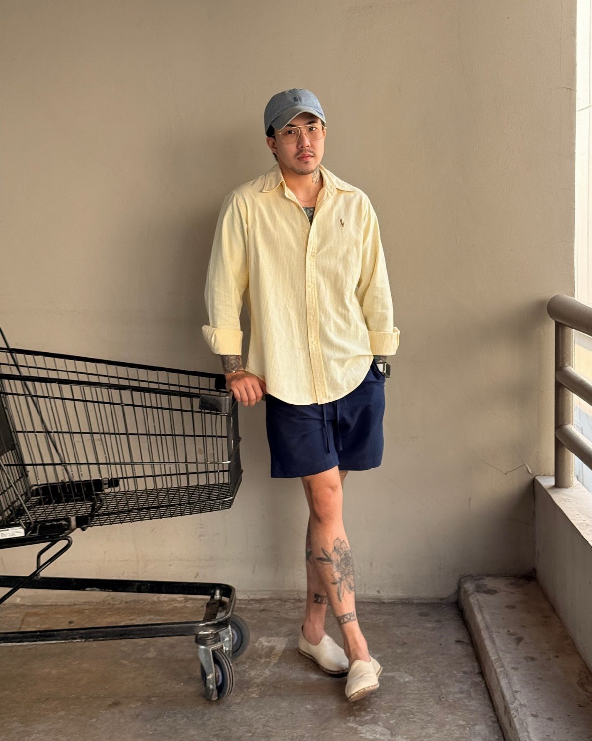 Man in yellow linen shirt and navy blue linen shorts leaning on shopping cart