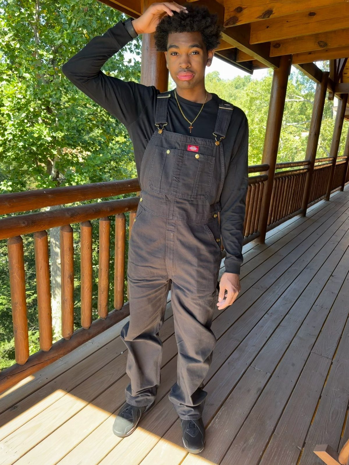 Young man wearing black overalls and a black long-sleeved shirt on a wooden deck