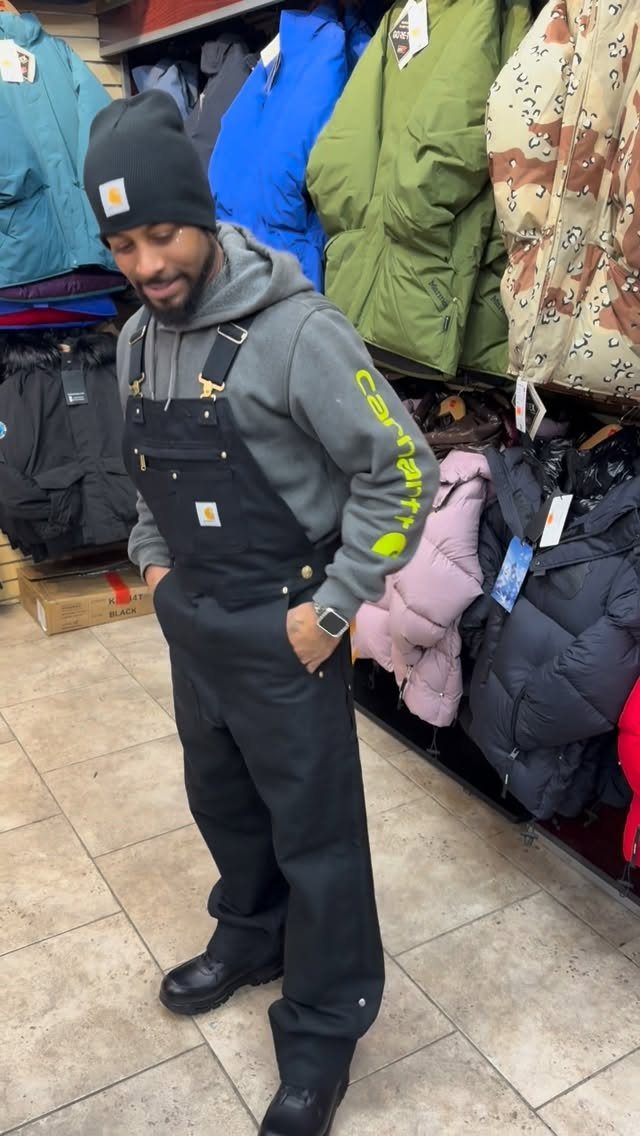 Man wearing black overalls, a grey hoodie, and a black beanie in a store