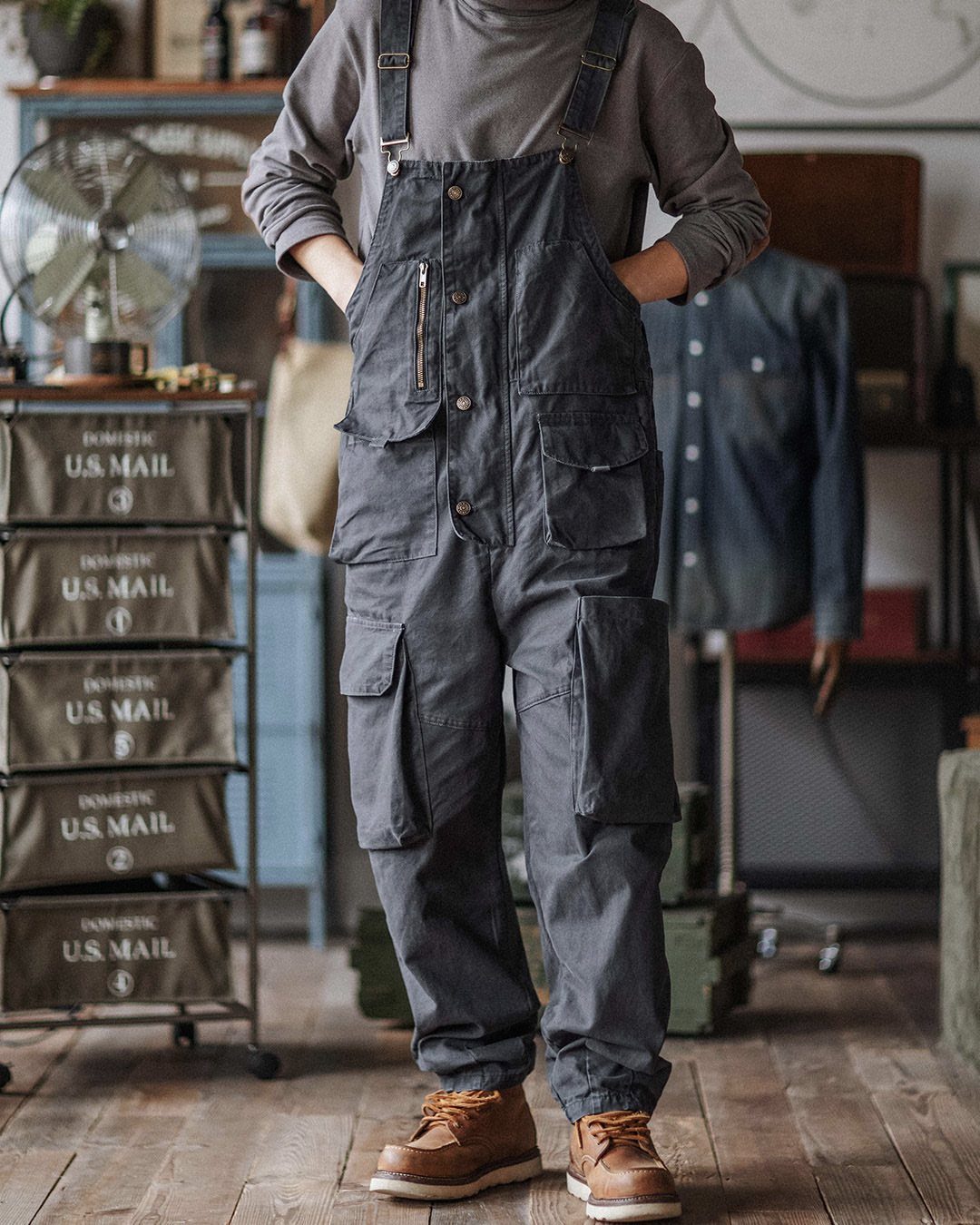 Man wearing dark grey overalls and brown boots in a rustic workshop setting