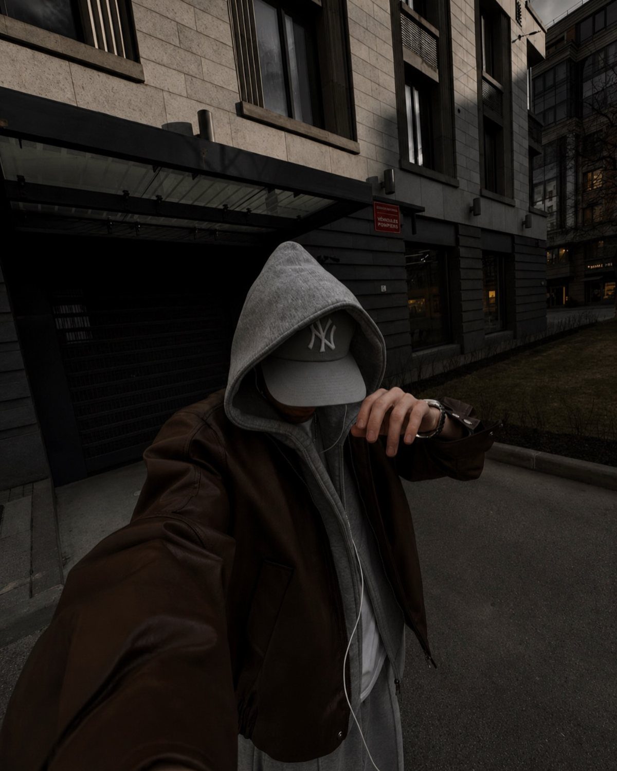 Person wearing a brown leather jacket over a grey hoodie and baseball cap.