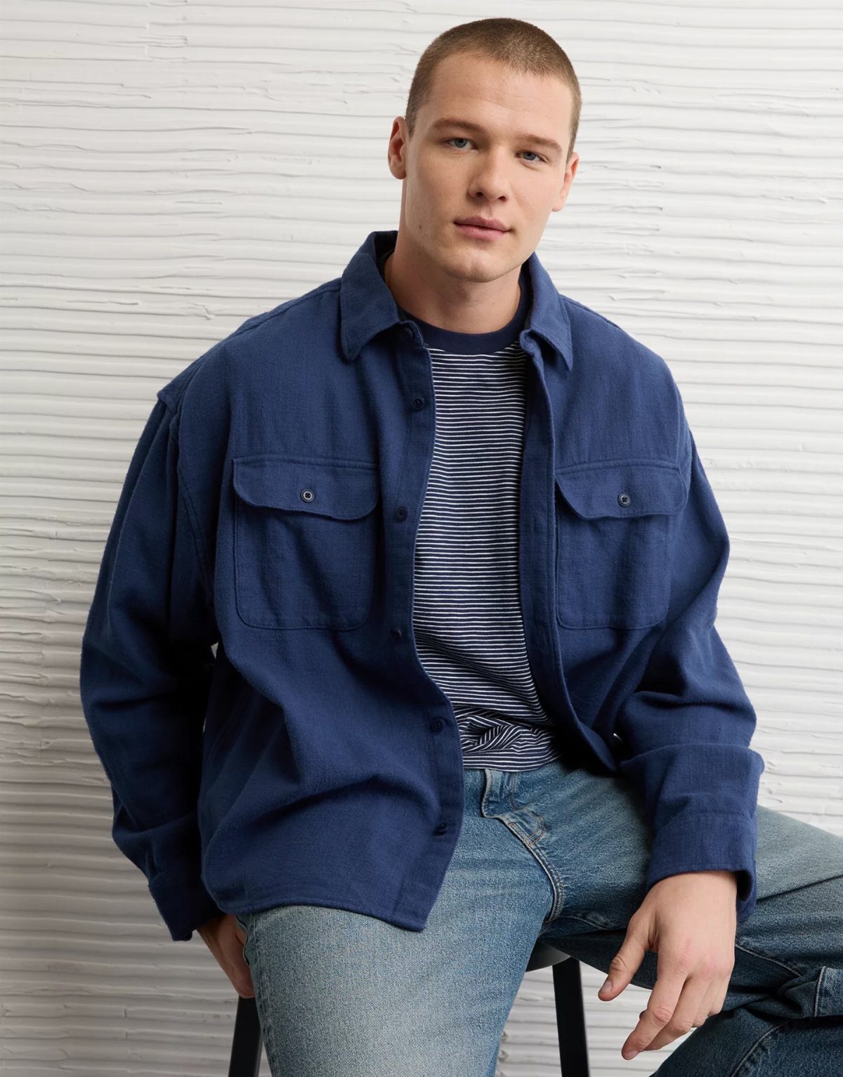 Man wearing a blue button-down shirt over a striped tee and light jeans.