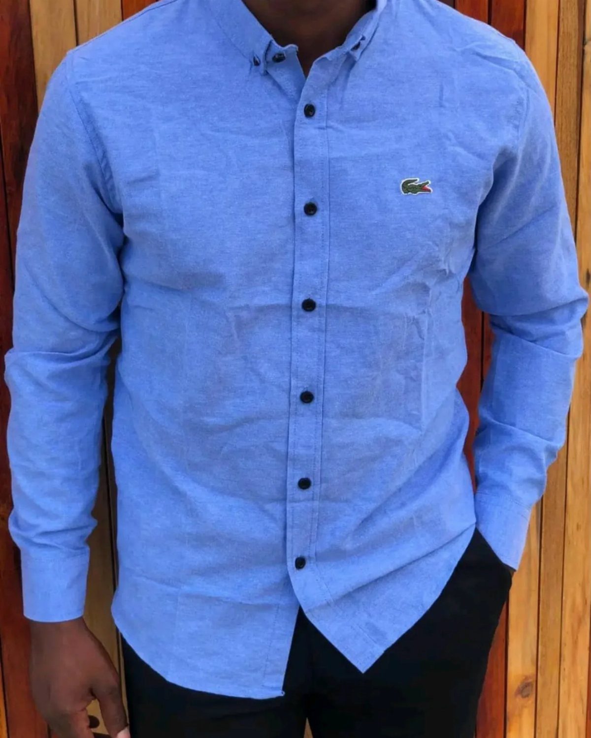 Man wearing a light blue long-sleeved button-down shirt and black trousers.