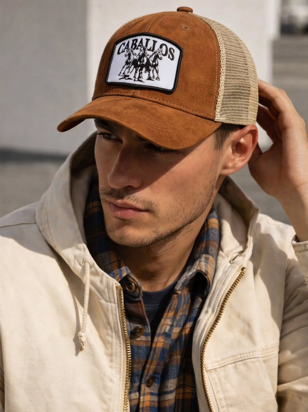 Man wearing a brown trucker hat with a patch and a cream hoodie.