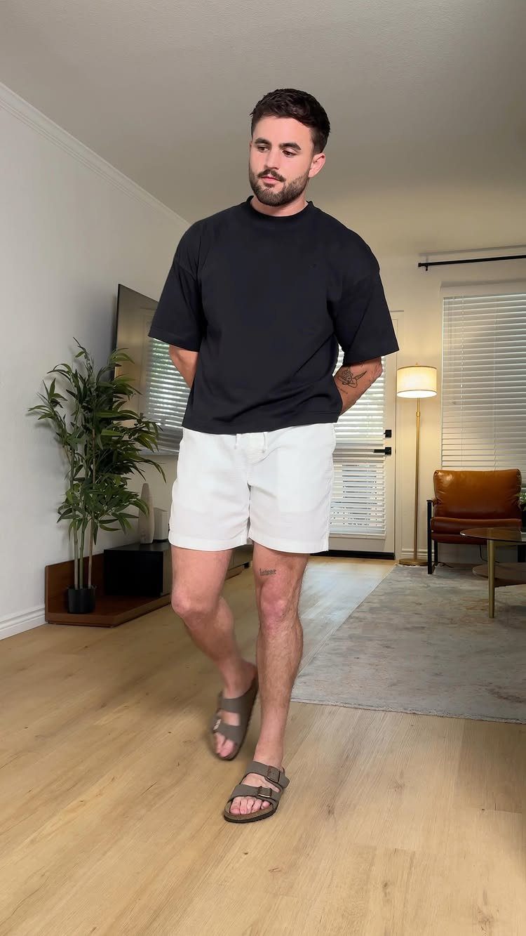 Man wearing a black t-shirt and white summer shorts in a living room