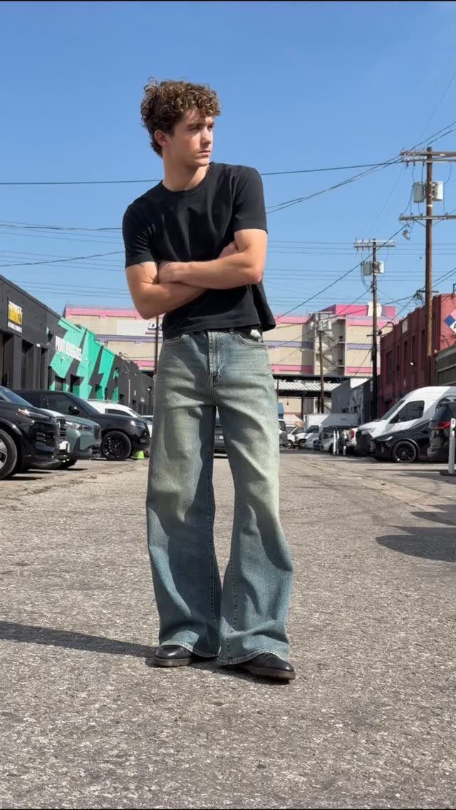 Man in black t-shirt and wide-leg blue jeans standing on a city street