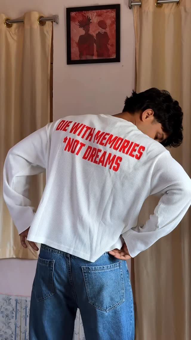 Man wearing a white long-sleeved textured shirt with red text and blue jeans.