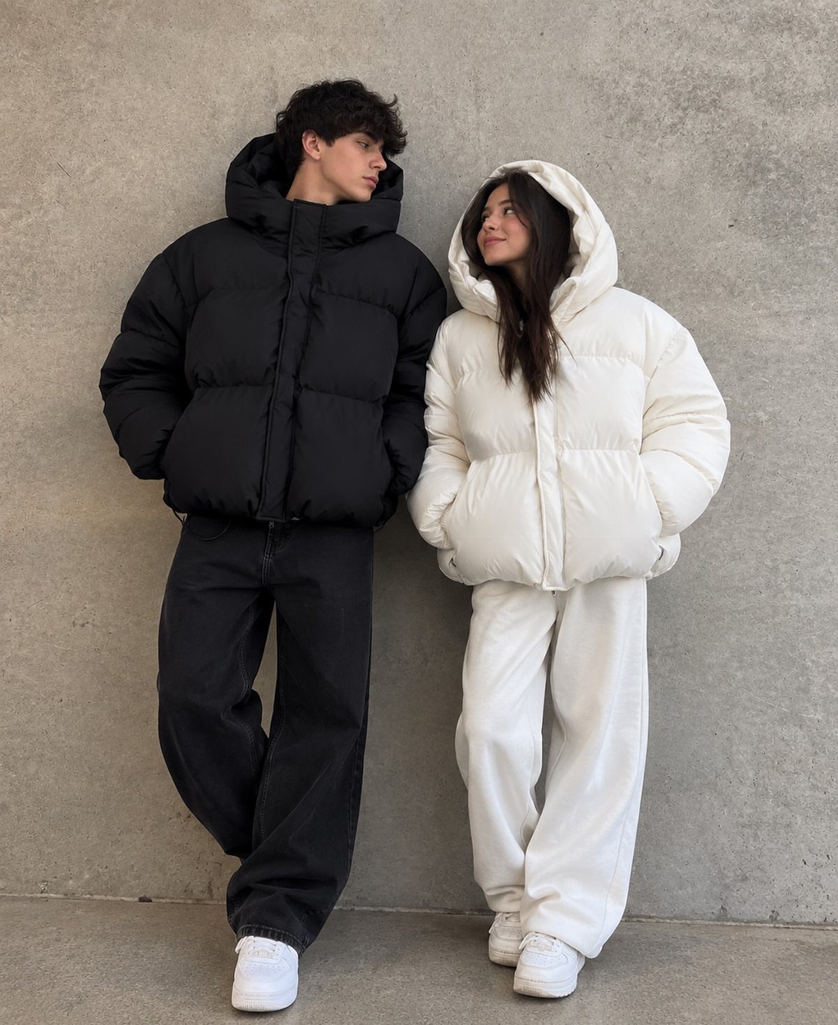 Man and woman wearing oversized black and white puffer jackets and matching trousers.
