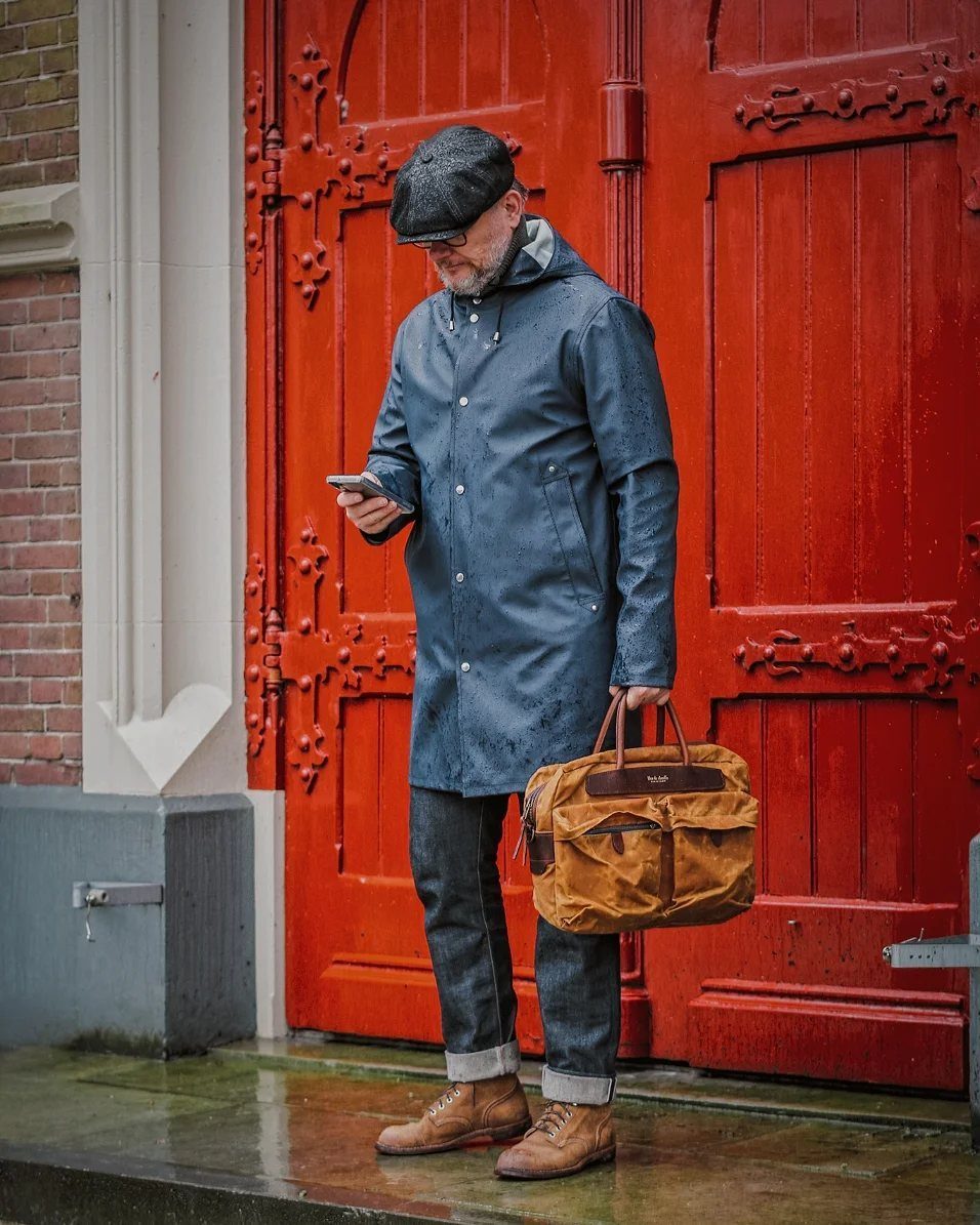 Man in blue hooded raincoat and jeans standing before a red door