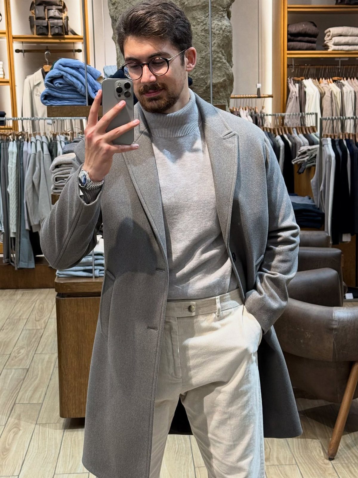 Man in grey overcoat and grey turtleneck sweater posing in a clothing store