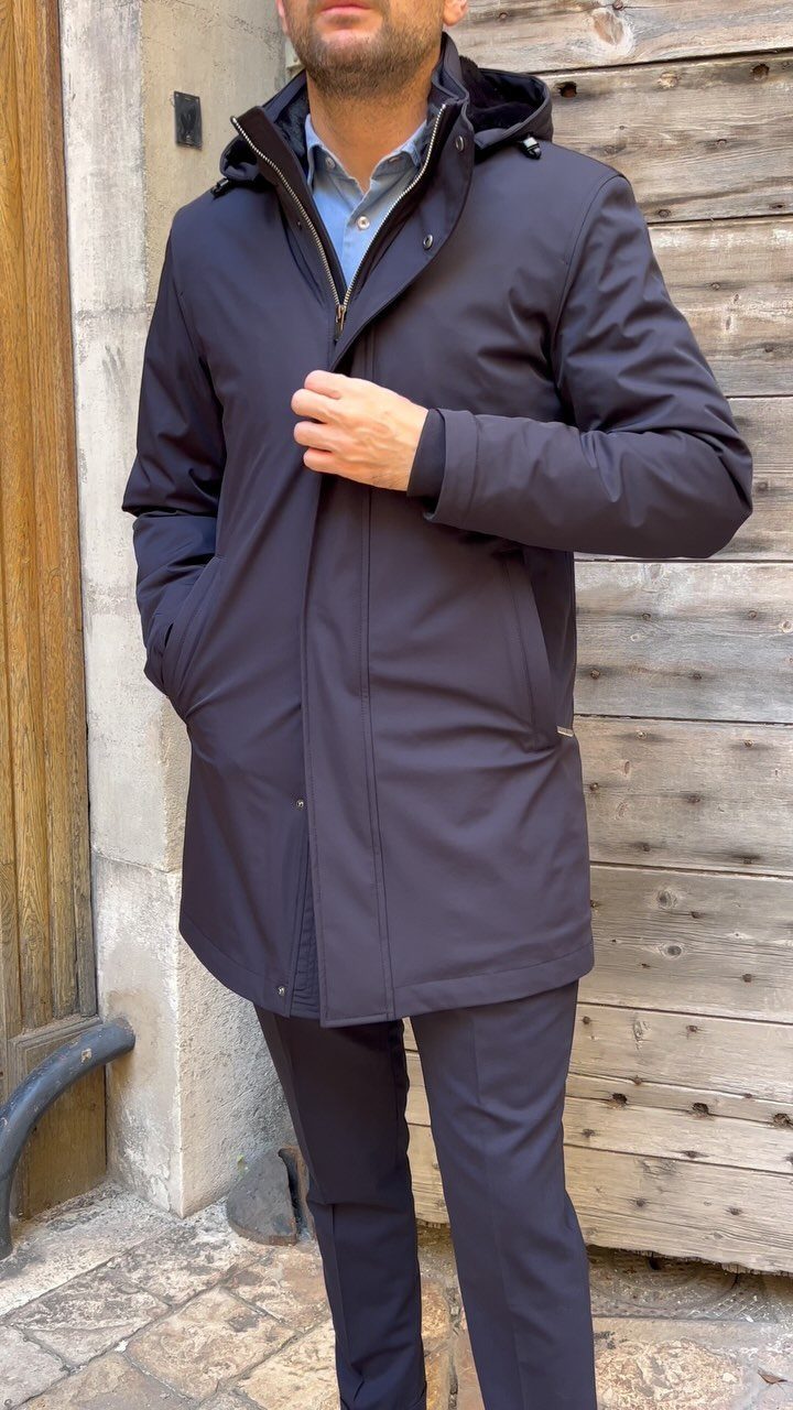 Man wearing a long black hooded parka with a blue shirt and trousers.