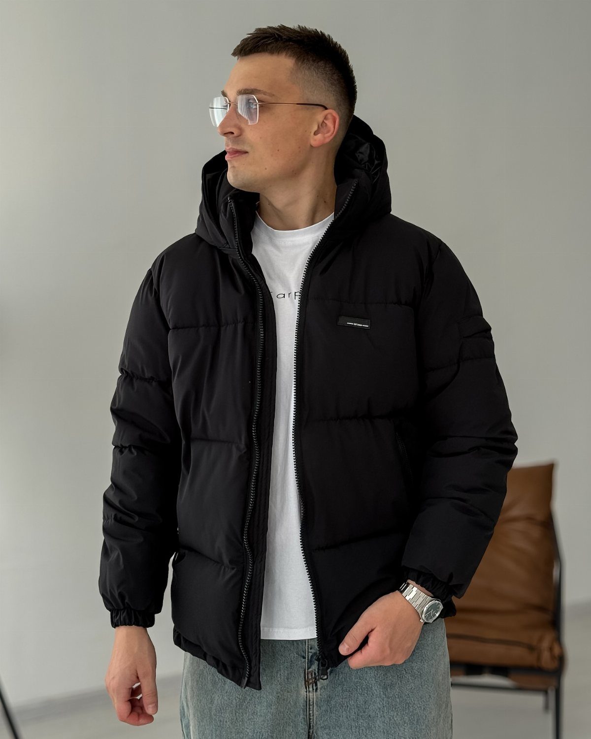 Man wearing a black hooded puffer jacket over a white t-shirt and jeans.