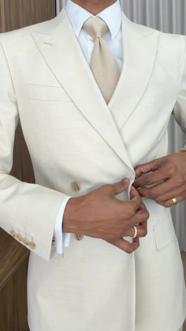 Man wearing a cream double-breasted suit with a white shirt and beige tie.