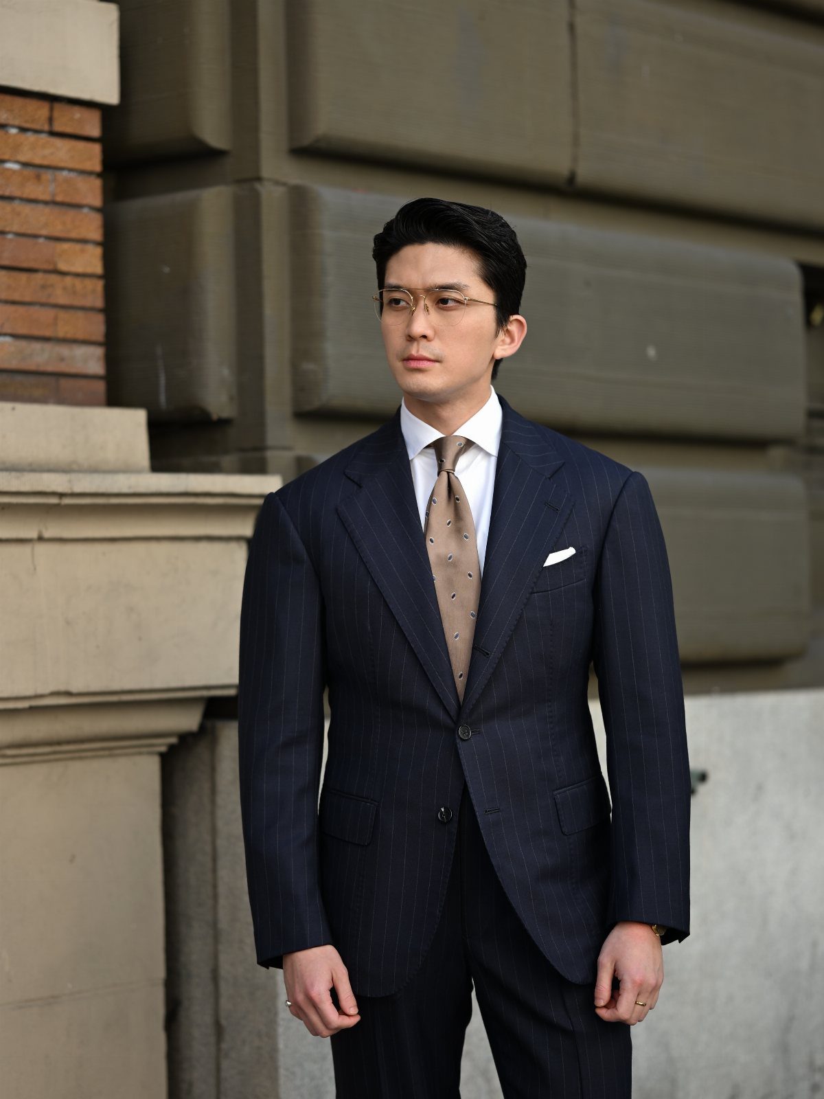 Man in a navy blue pinstripe single-breasted suit with a gold patterned tie.