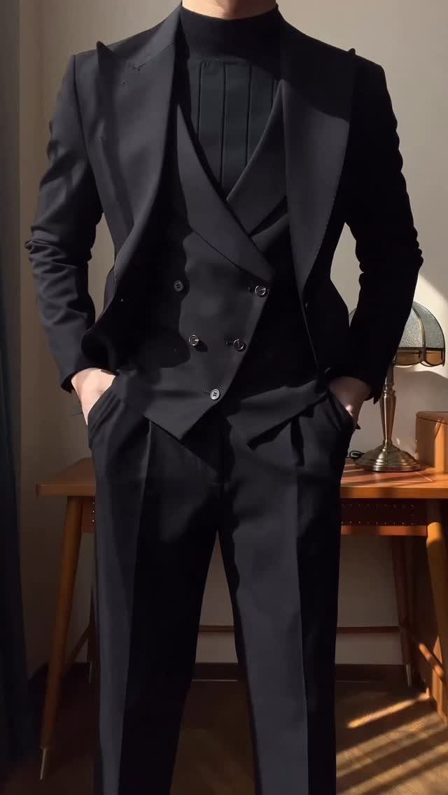 Man wearing a navy blue three-piece suit with a dark turtleneck sweater indoors.