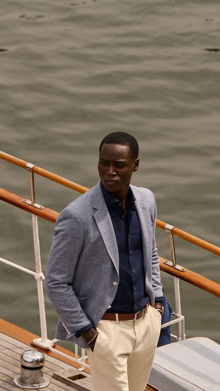 Man in a blue blazer and beige chinos standing on a boat deck.