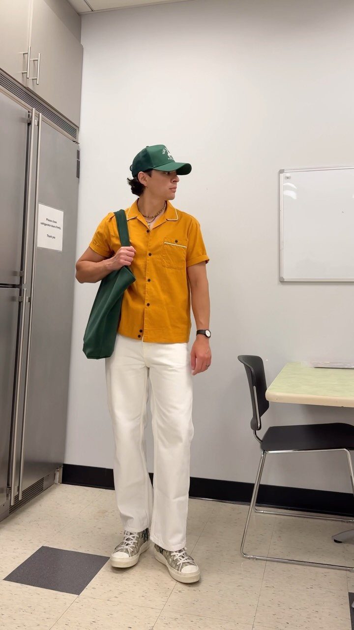 Man in mustard camp collar shirt, white trousers, and green baseball cap.