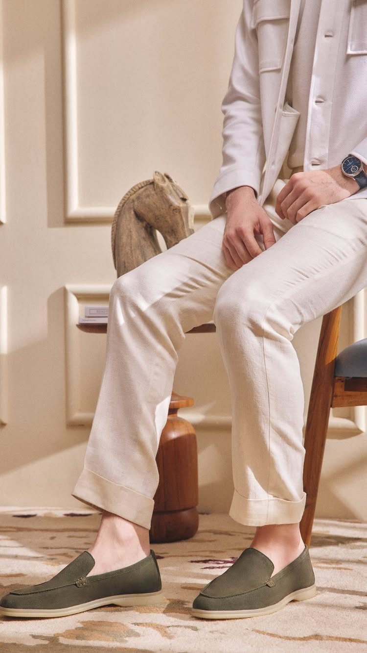 Olive green suede loafers worn with cuffed off-white trousers and a white shirt.