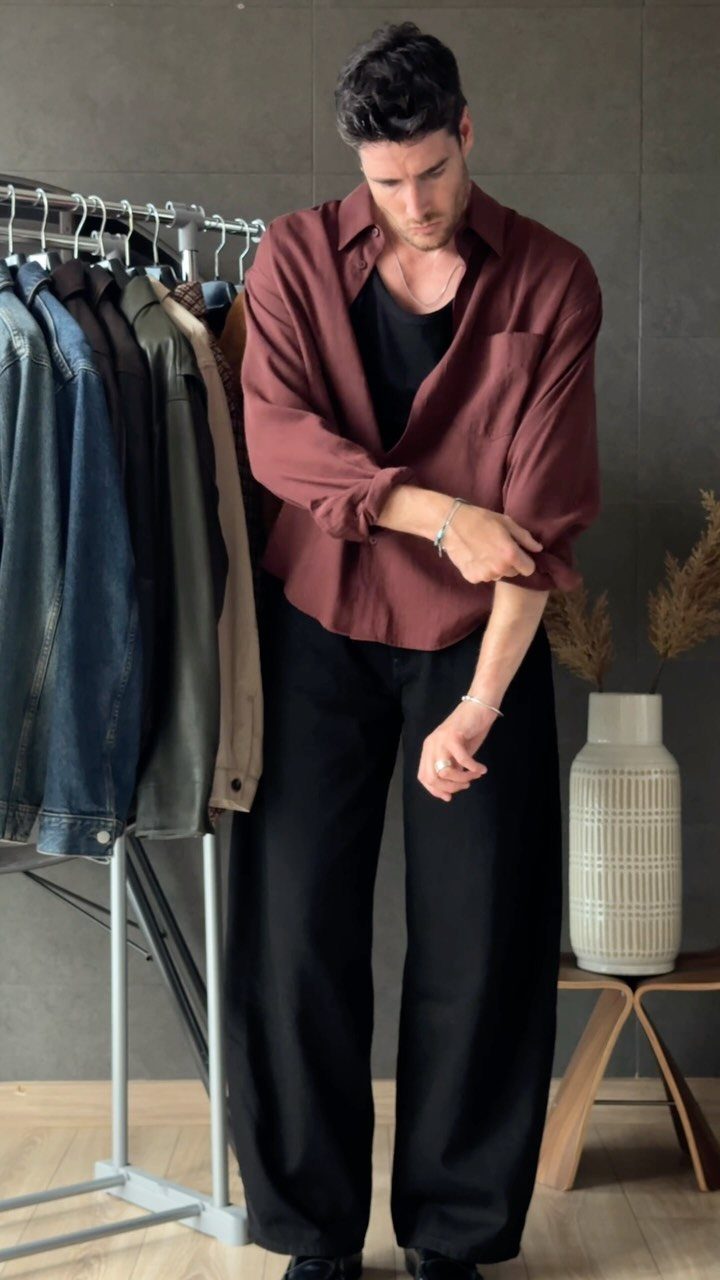 Man wearing a maroon open shirt over a black tee and wide black trousers.