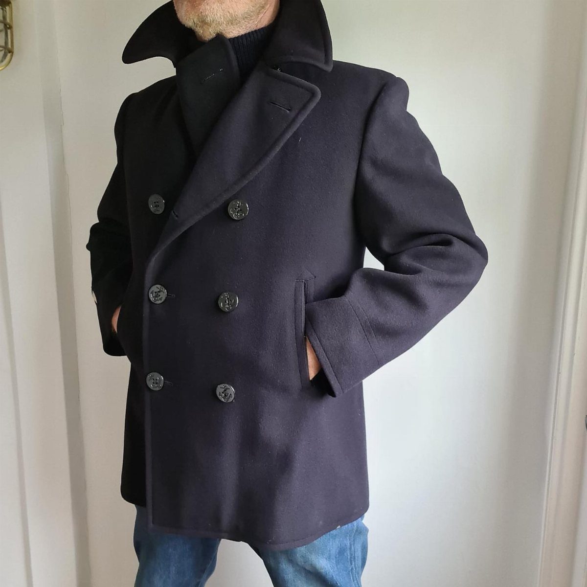 Man wearing a navy blue double-breasted wool peacoat with blue jeans