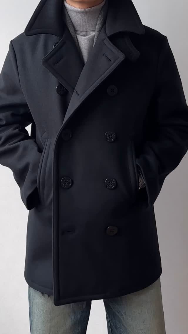 Man wearing a navy blue double-breasted peacoat with a grey turtleneck and jeans.