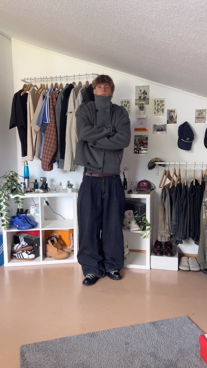 Man wearing a grey peacoat and wide dark trousers standing in a dressing room