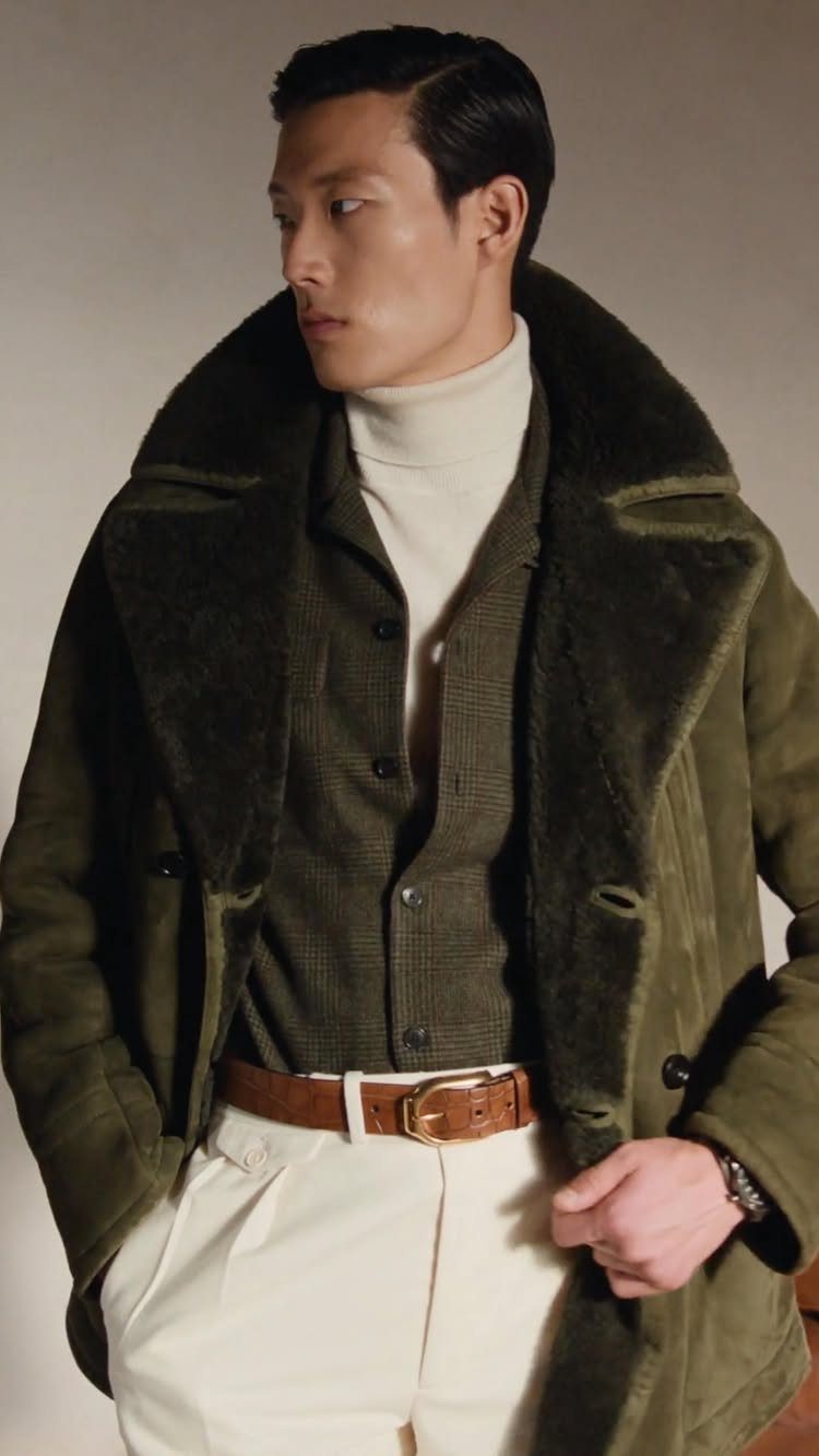 Man wearing an olive green shearling peacoat with white trousers and brown belt.