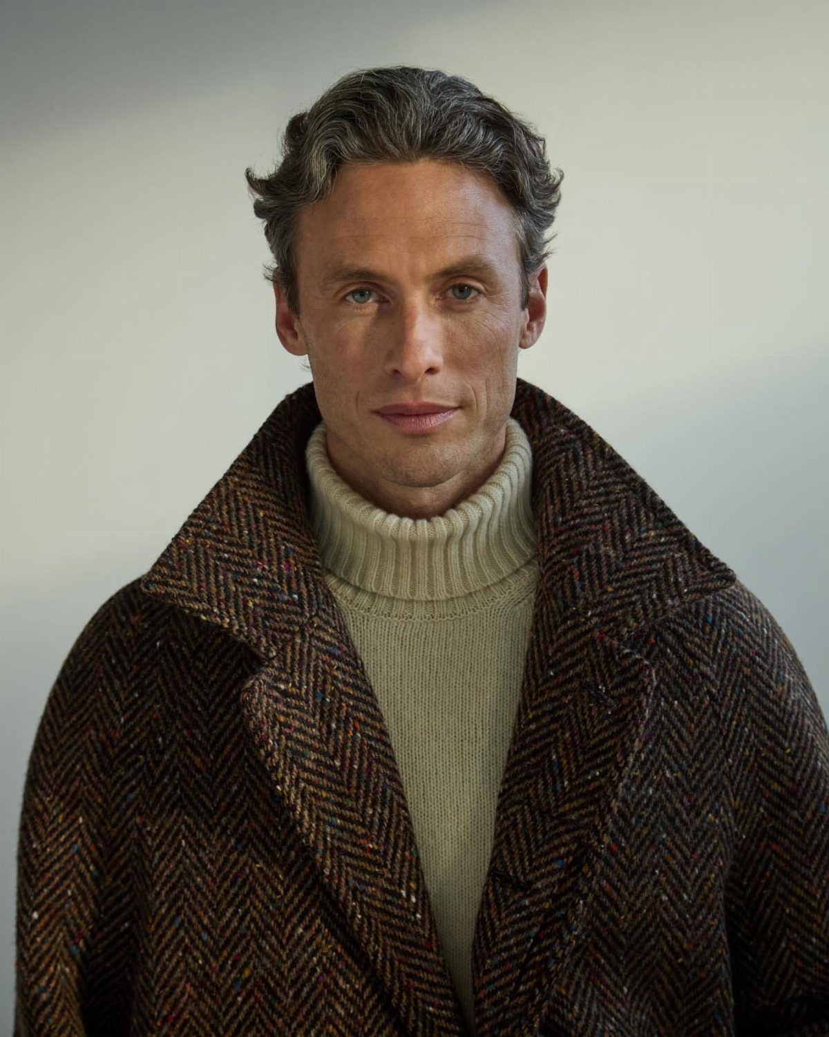 Man wearing a brown herringbone wool coat and a cream turtleneck sweater.