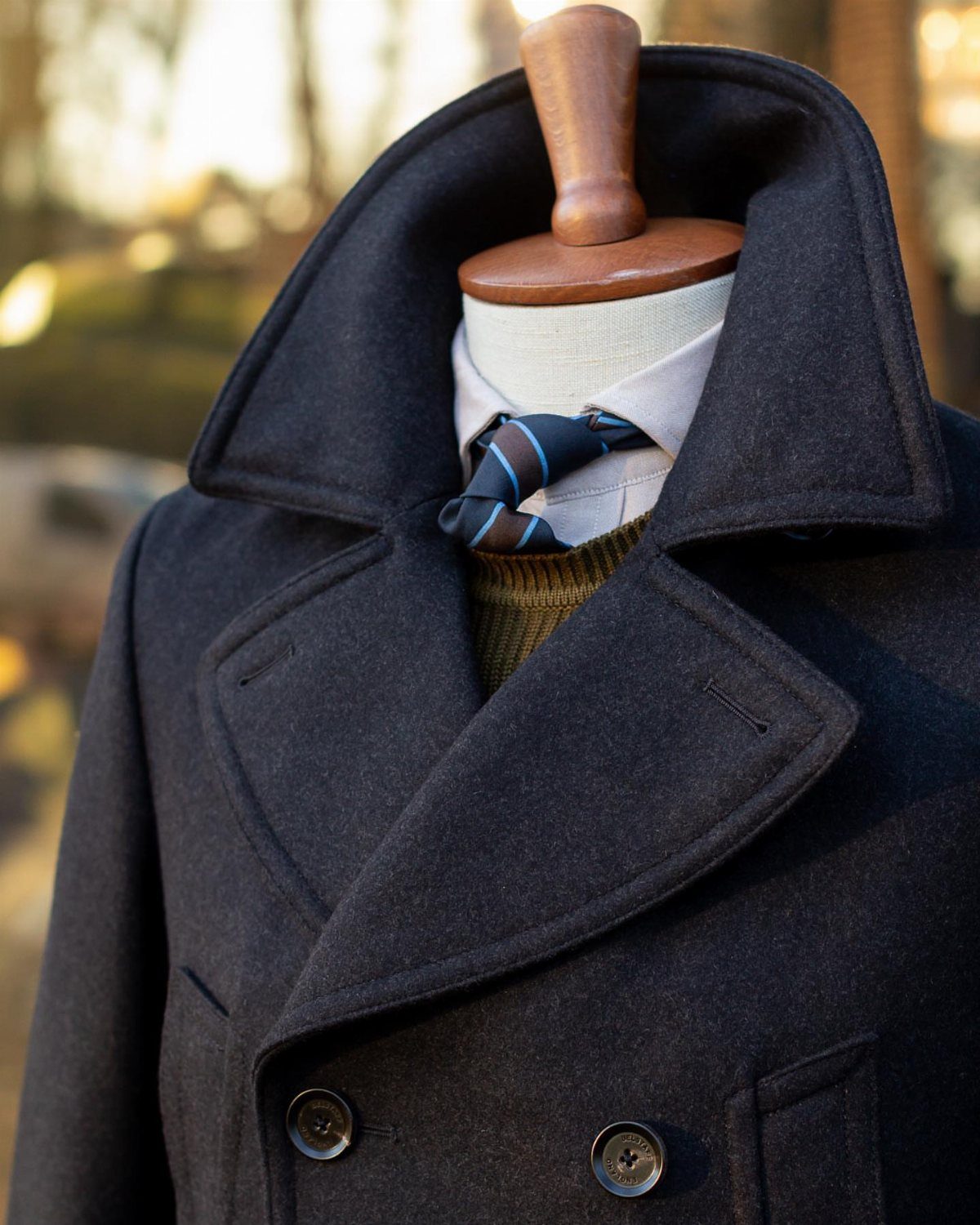 Navy blue wool coat on a mannequin with a tie and sweater.