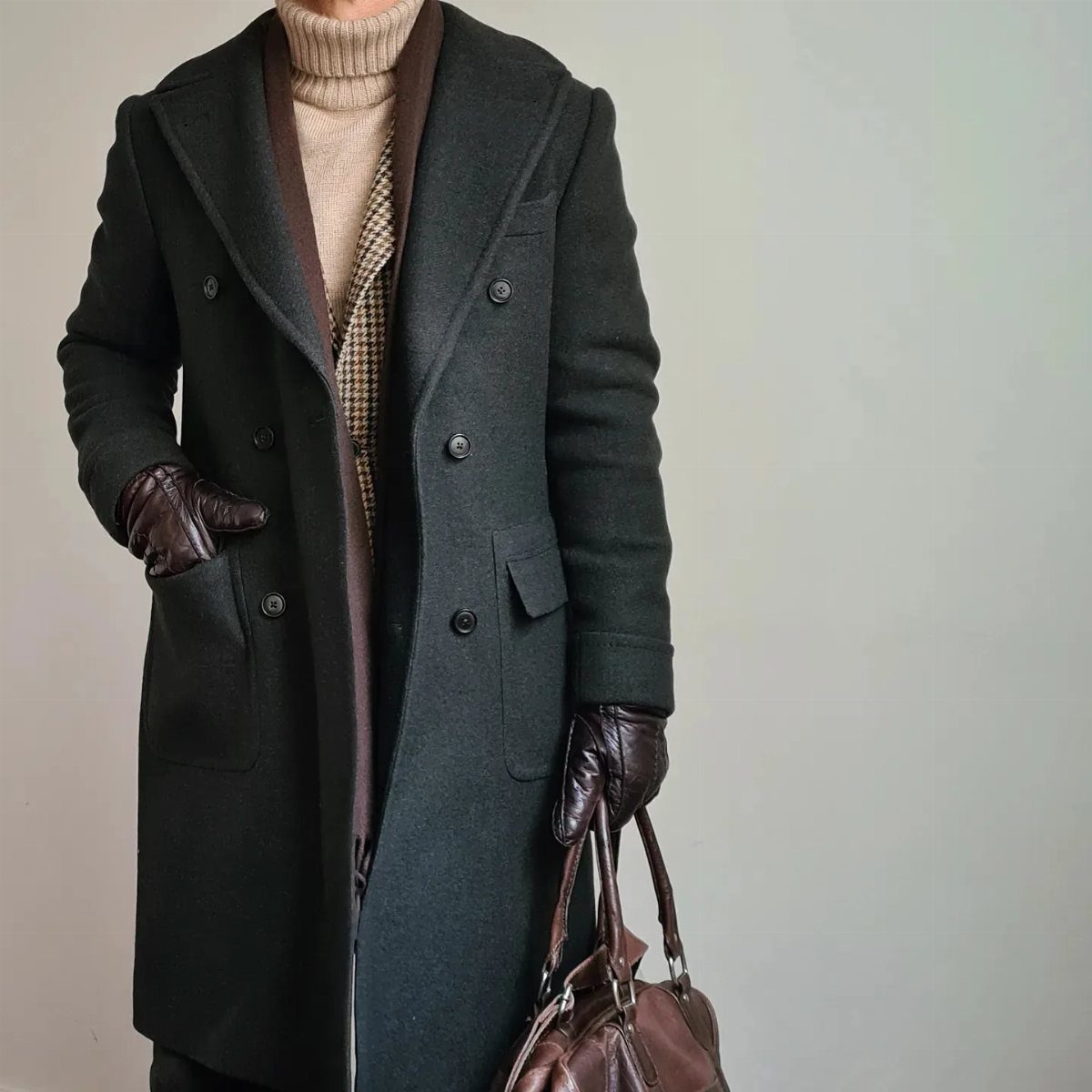 Dark charcoal grey double-breasted wool coat worn with beige turtleneck and leather gloves.