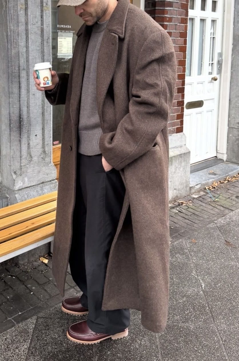 Man in a long brown wool coat holding coffee on a city street